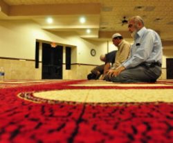 A few men pray together in a large, quiet room.