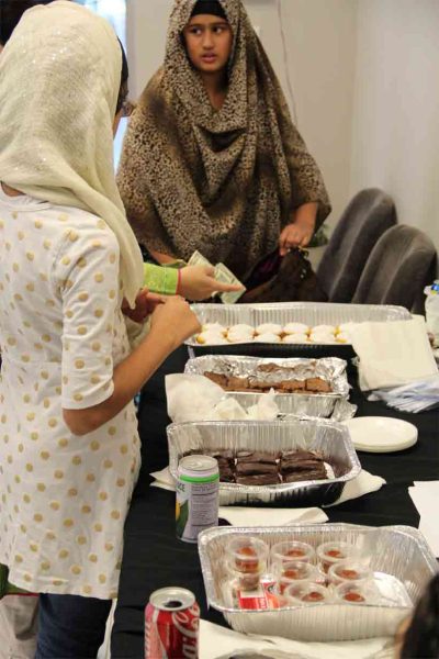 Sweets line a table as hijabis purchase.