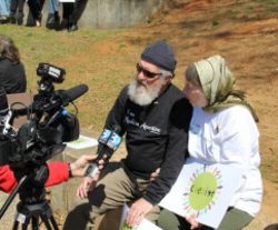 A Muslim couple is interviewed by several cameras representing different media outlets at the park.