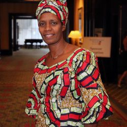 Rose Mapendo stands outside of a banquet hall wearing a boldly printed African style dress and head wrap.