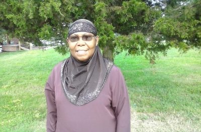 Sister Aquila, an African-American woman, stands wearing a black hijab and long shirt while in a lush yard. This photo was taken after her talk during the Ramadan Sessions.